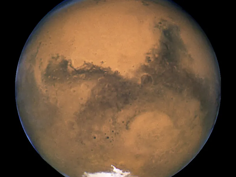 Mars seen from space: a reddish-orange globe with dark markings and a white polar cap