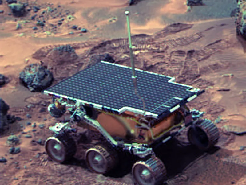 A small six-wheeled rover beside a rock on reddish ground